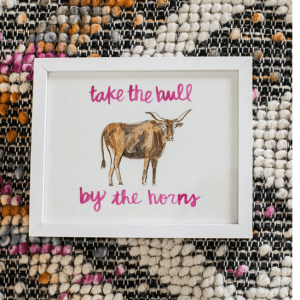 woven background, with a framed image of a bull, with the captions "take the bull" on top and "by the horms" below the bull