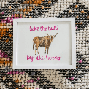 woven background with a framed image of a bull, with the captions "take the bull" on top and "by the horms" below the bull