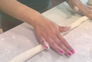 a woman's hand rolling elongated dough on table